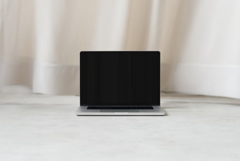 Silver laptop with blank black screen on light wooden desk