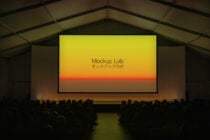 Large projection screen in auditorium showing sunset gradient with Mockup Lab text