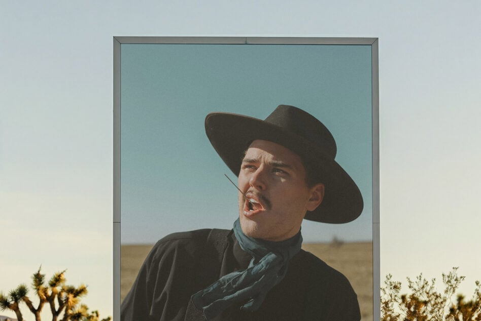 Outdoor billboard framing man in cowboy hat against desert landscape