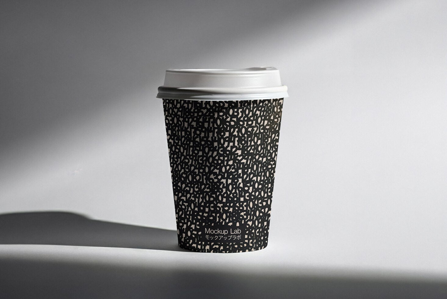 Black patterned coffee cup with white lid casting sharp shadow on surface