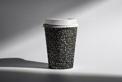 Black patterned coffee cup with white lid casting sharp shadow on surface