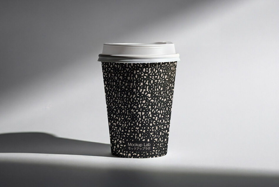 Black patterned coffee cup with white lid casting sharp shadow on surface