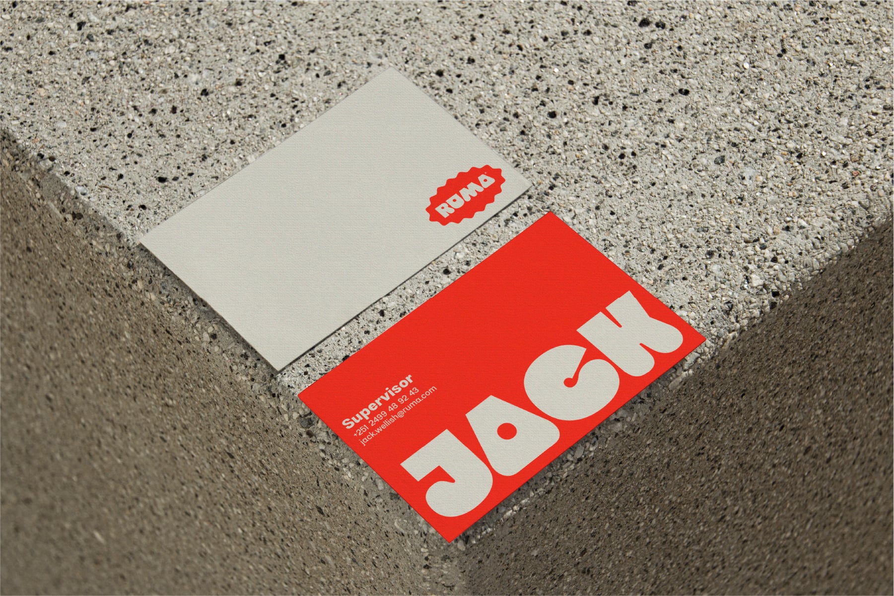 Red business cards with ROMA logo on speckled concrete surface