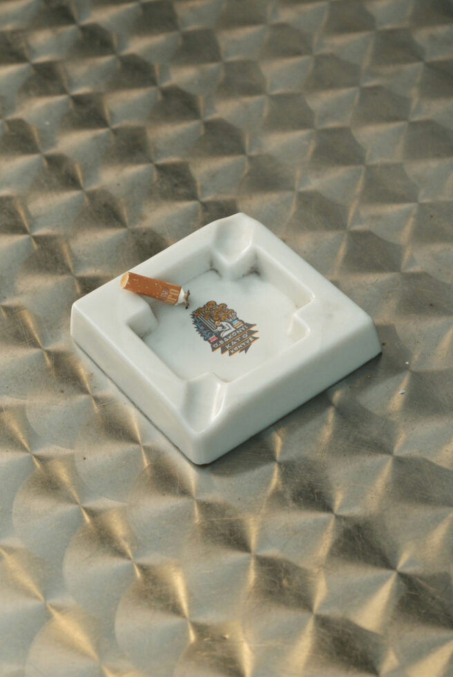 White marble ashtray with lit cigarette on textured stone surface