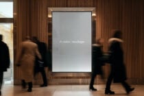 Large illuminated display frame mounted on wood wall with blurred people walking past