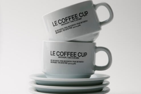 Two ceramic mugs with Le Coffee Cup text stacked on matching saucers