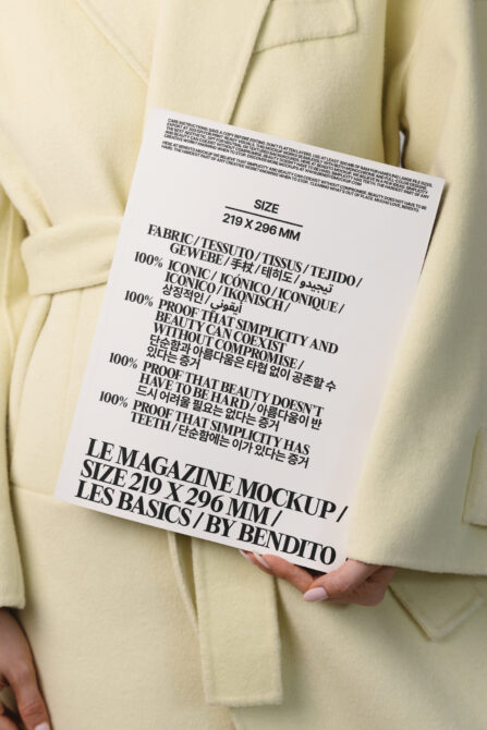 White magazine held in hands against cream blazer, black typography visible