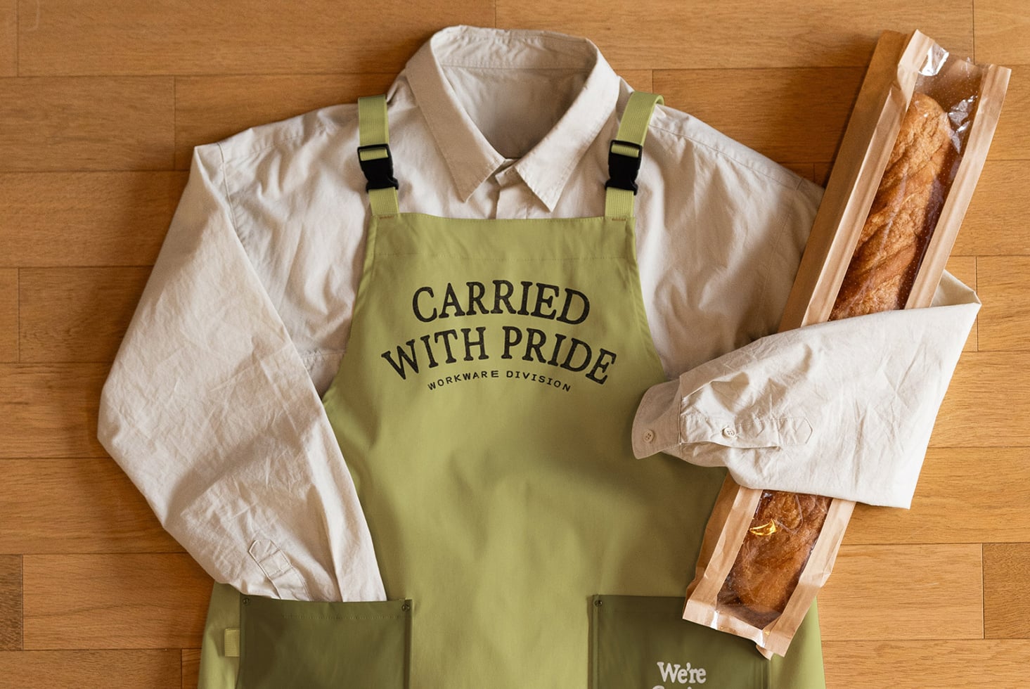 Lime green apron flat lay styled with cream shirt, black straps, bread
