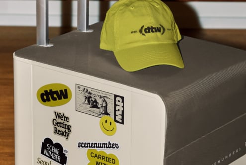 Lime yellow baseball cap with atw logo stacked on white suitcase covered in brand stickers