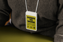 Yellow ID badge Down to Work text worn on white cord over brown jacket