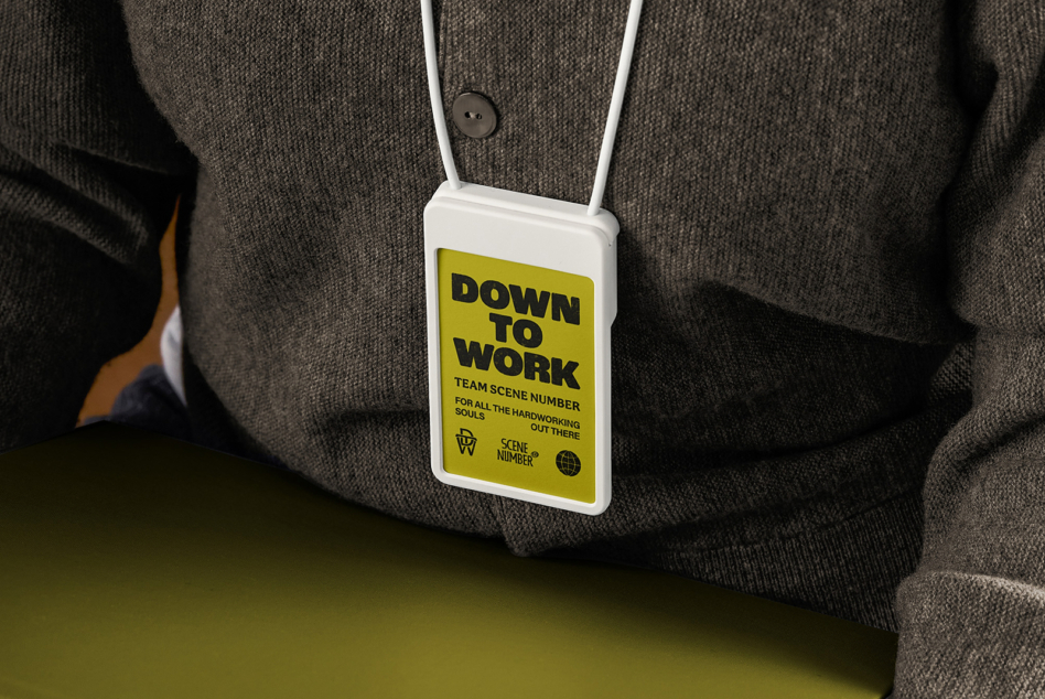 Yellow ID badge Down to Work text worn on white cord over brown jacket