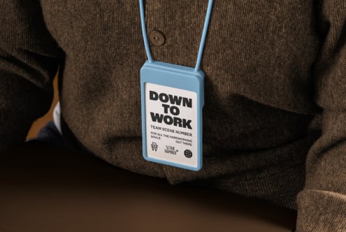 Light blue ID badge with Down to Work text on white cord over brown vest