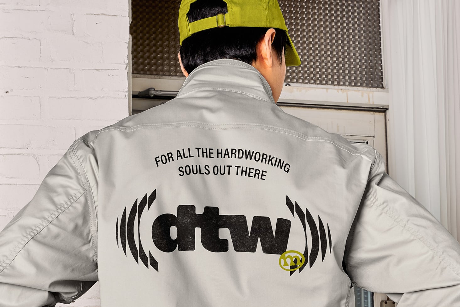 Cream windbreaker back view with workwear graphic, neon yellow cap visible