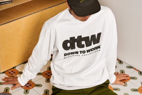 Overhead of guy in black cap wearing cream sweatshirt with dtw logo on floor