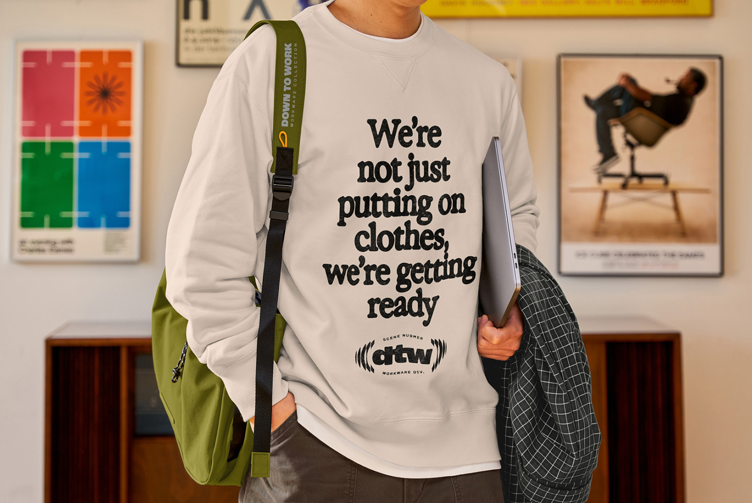 Guy wearing cream sweatshirt with bold black text, olive shoulder bag, holding laptop