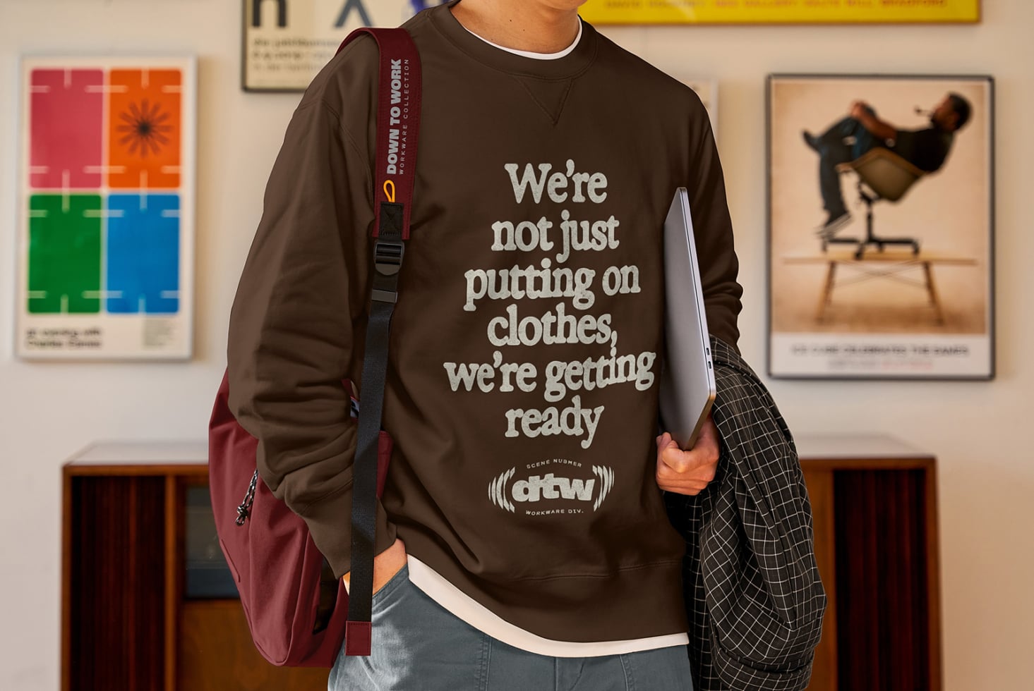 Model in brown sweatshirt carrying burgundy shoulder bag, holding silver laptop
