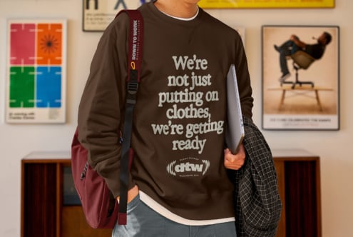 Model in brown sweatshirt carrying burgundy shoulder bag, holding silver laptop