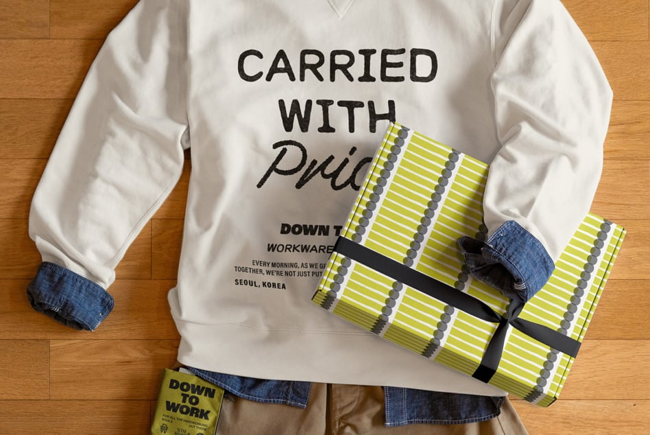 Person holding yellow patterned clutch wearing white sweatshirt with Carried with Pride design