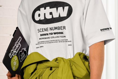 White t-shirt displaying Down to Work Scene Number design, held with black branded bag