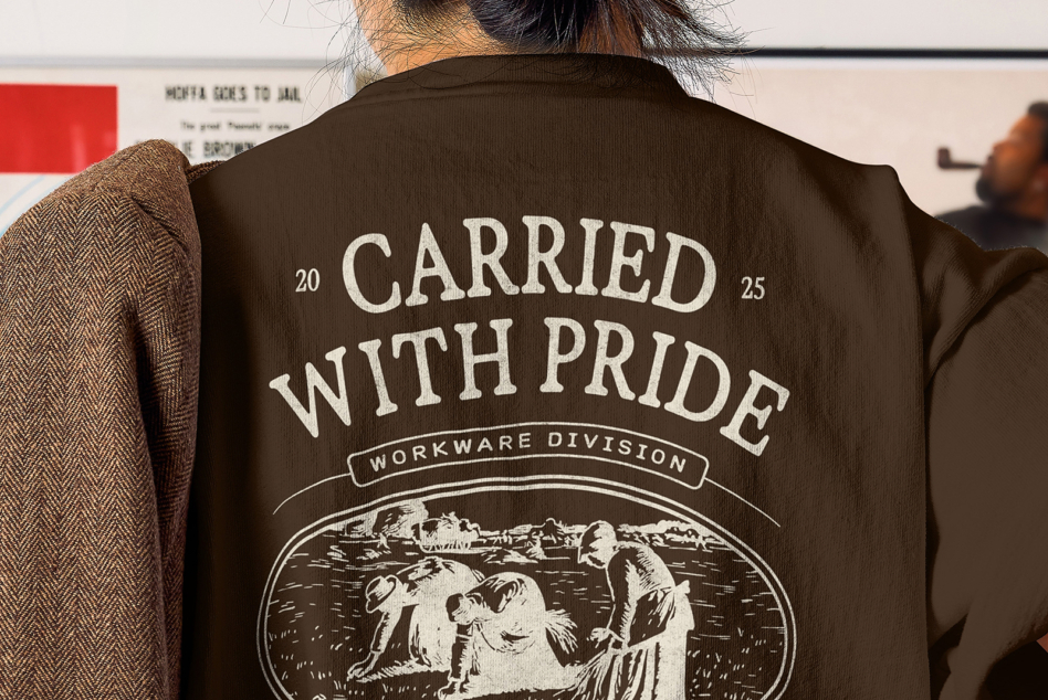 Dark brown tee with large Carried With Pride text over engraved pastoral scene art