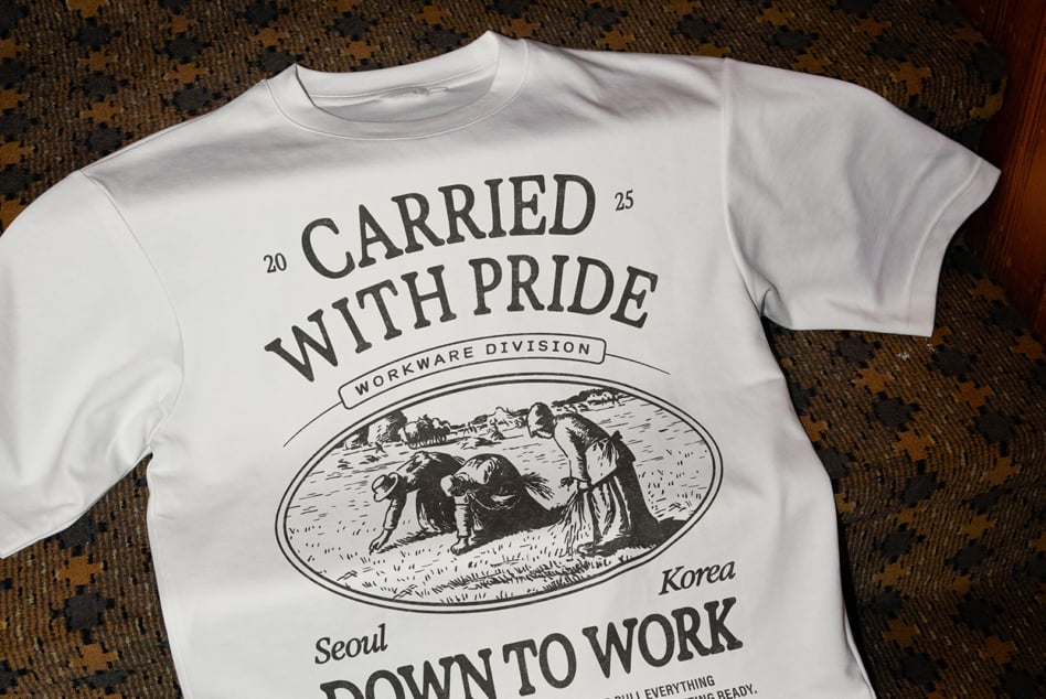 White tee with vintage workwear graphic saying Carried With Pride, worn flat lay