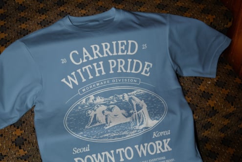 Blue tee with large Carried With Pride workwear engraving on patterned rug