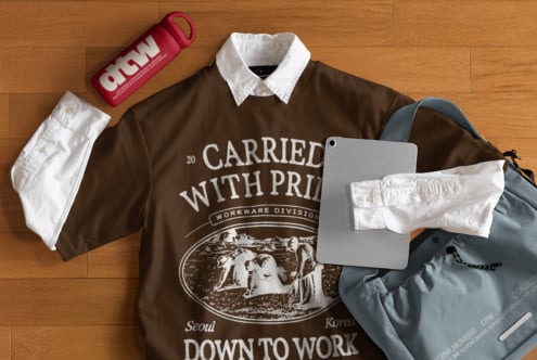 Brown oversized tee with white collar, pink speaker, slate bag on wood floor