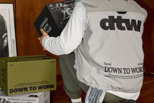 Worker in cream jacket holding black envelope near stacked boxes on floor