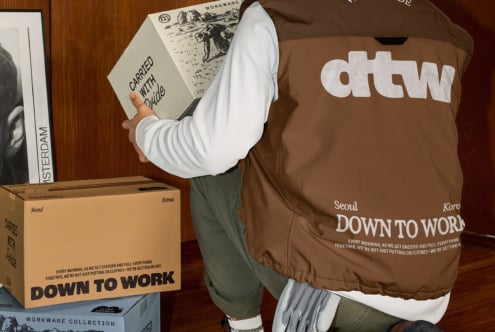 Person in brown puffer jacket holding cream envelope against wood wall backdrop