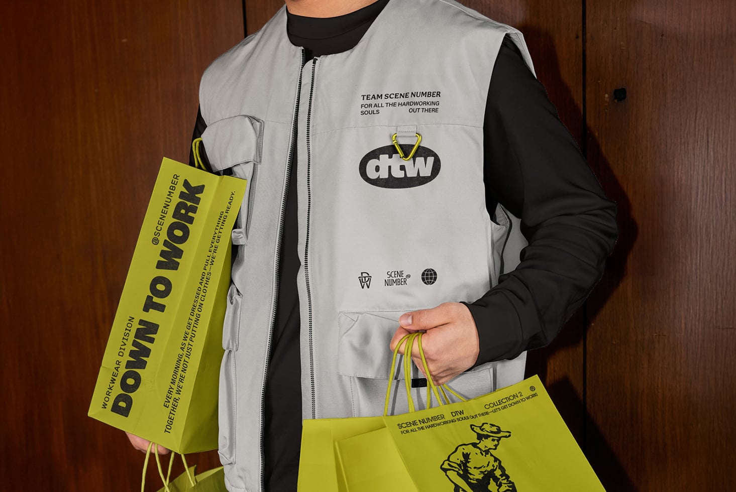Person in gray vest with DTW logo holding bright yellow shopping bags with design