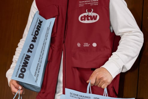 Burgundy vest with white dtw logo over white shirt, holding light blue branded paper bag on model