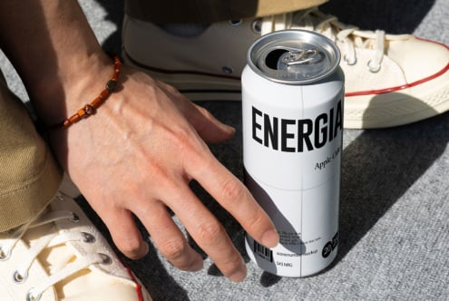 Person in sneakers holding Energia apple cider can on concrete ground
