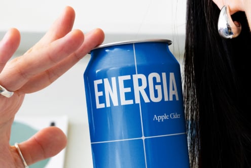 Blue Energia can held up against cloudy sky with person wearing silver drop earring