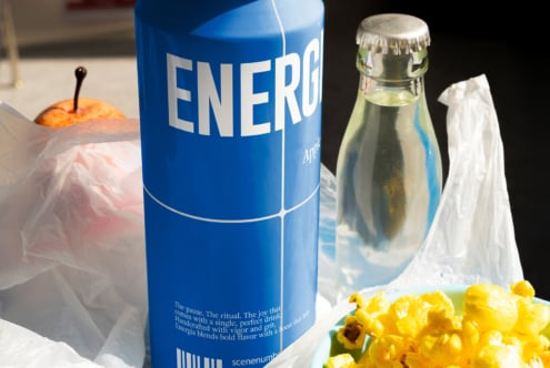 Blue Energia can on table with glass bottle, orange slice, yellow flowers in sunlight