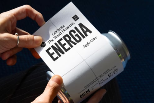 Hand holding white ENERGIA can with Apple Cider text on dark backdrop