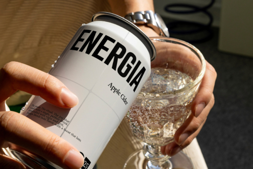 Person holding white energy drink can next to filled glass of bubbly drink