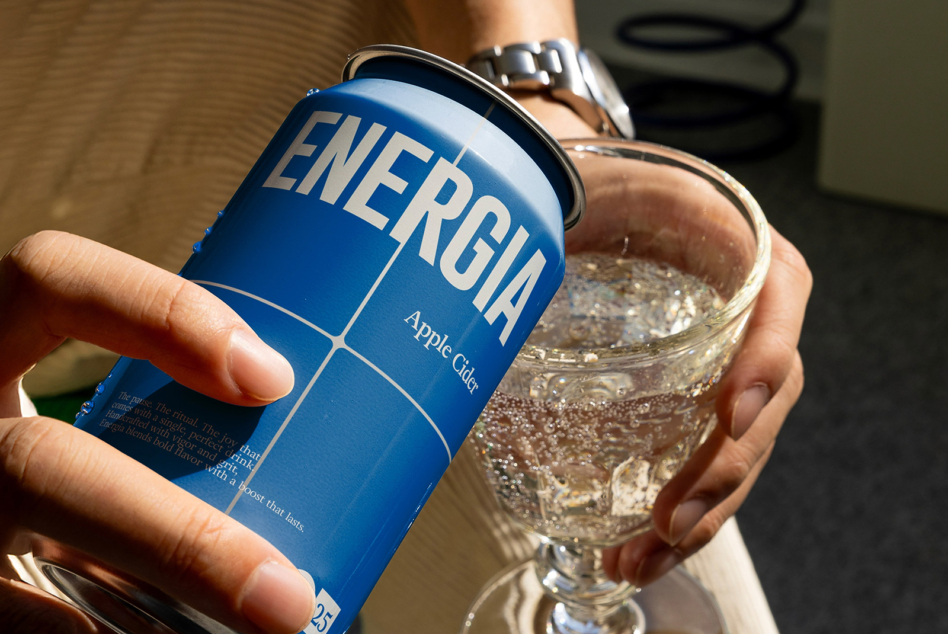 White canned energy drink next to fizzy drink in glass with watch visible