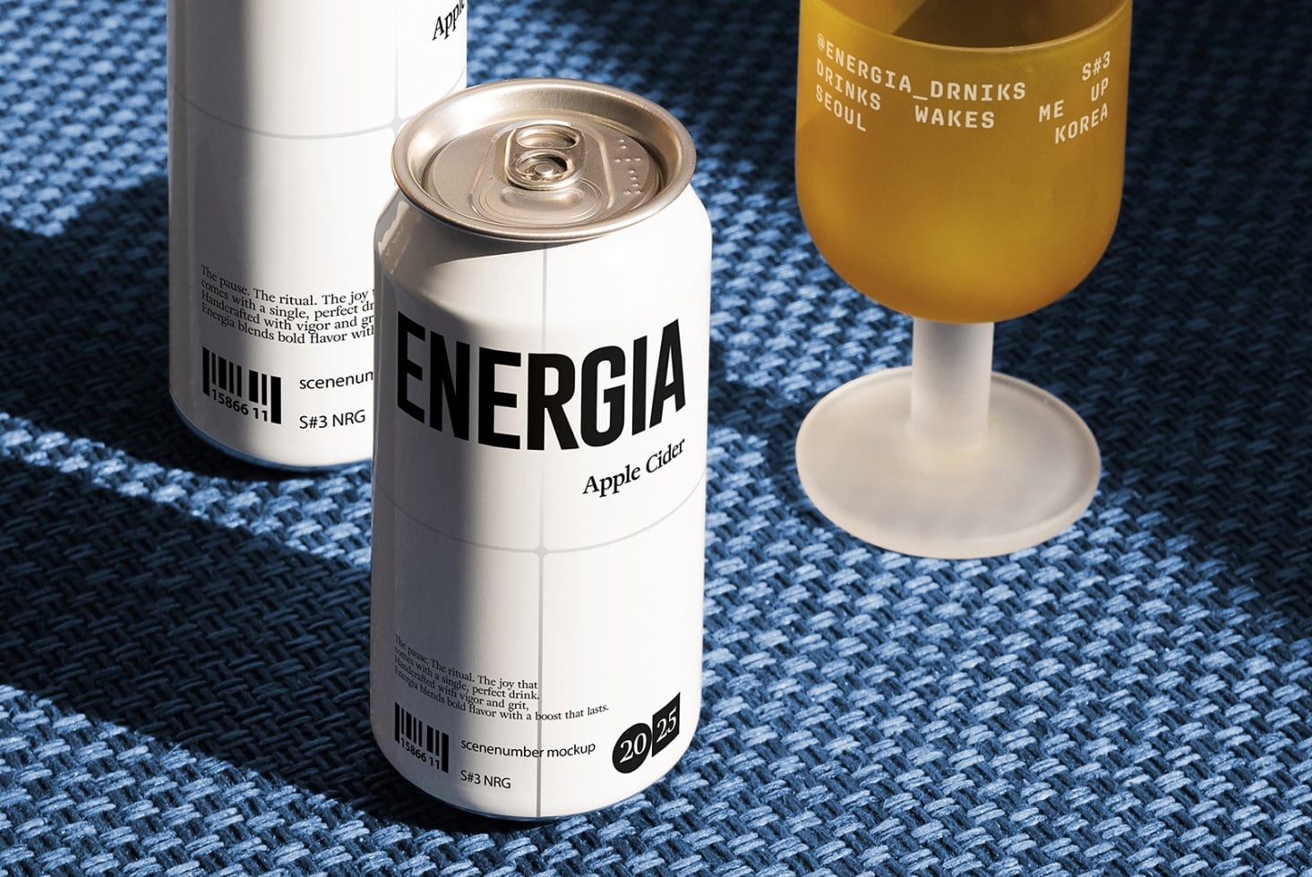 Energia apple cider can with white version, glass of liquid, blue fabric backdrop