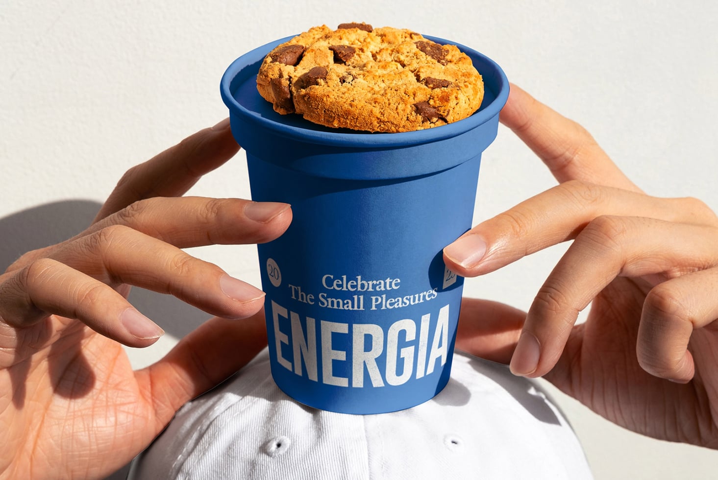 Hands holding blue cup with chocolate chip cookies, Energia branding visible