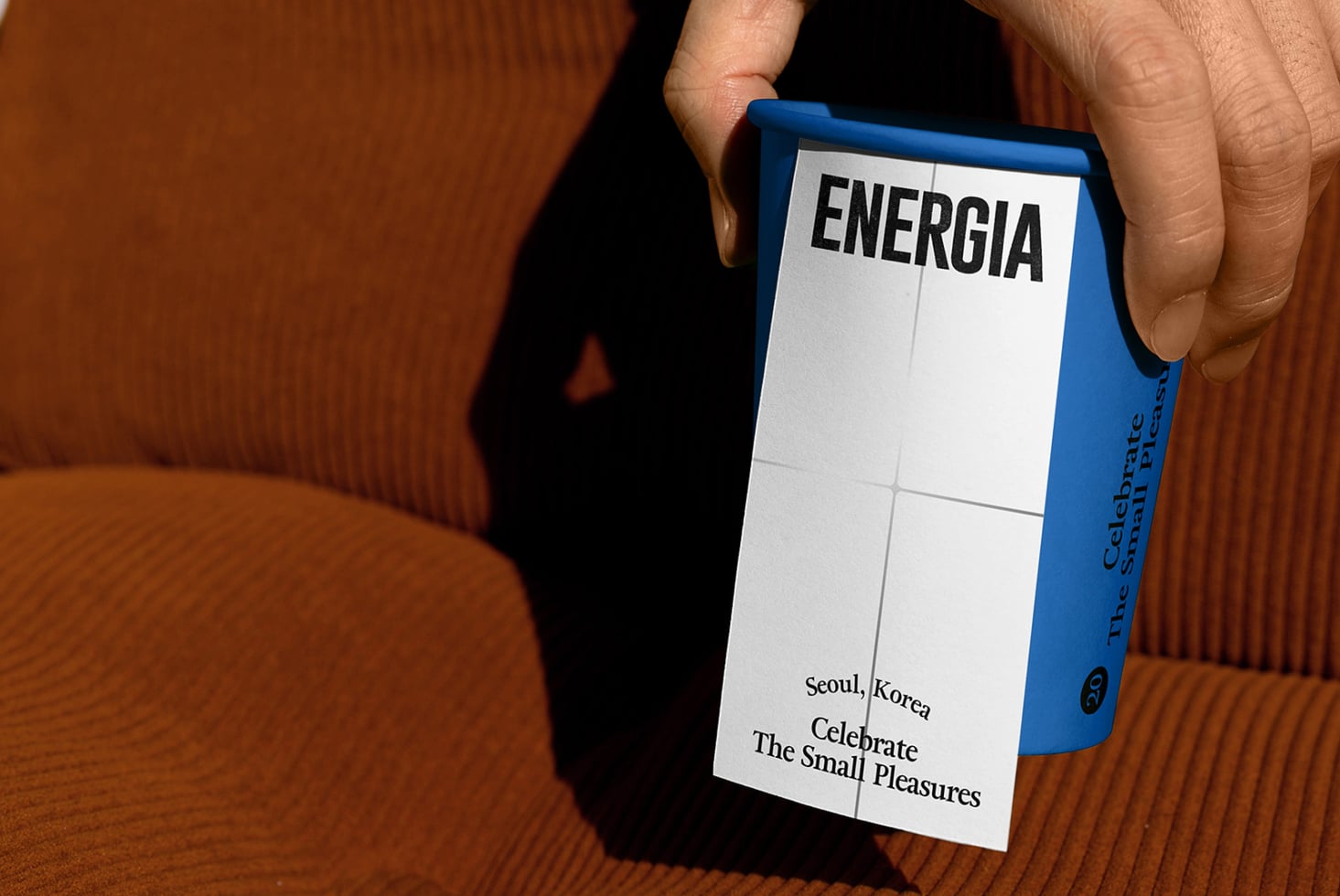 Hands holding blue box with ENERGIA text, white panel detail, textured brown background