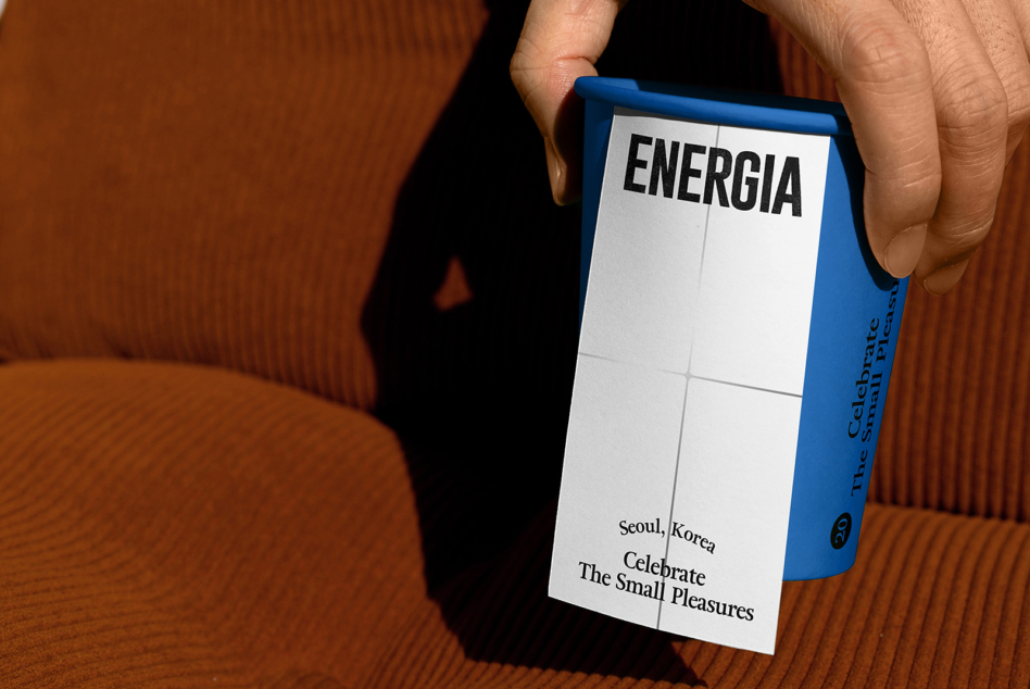 Hands holding blue box with ENERGIA text, white panel detail, textured brown background