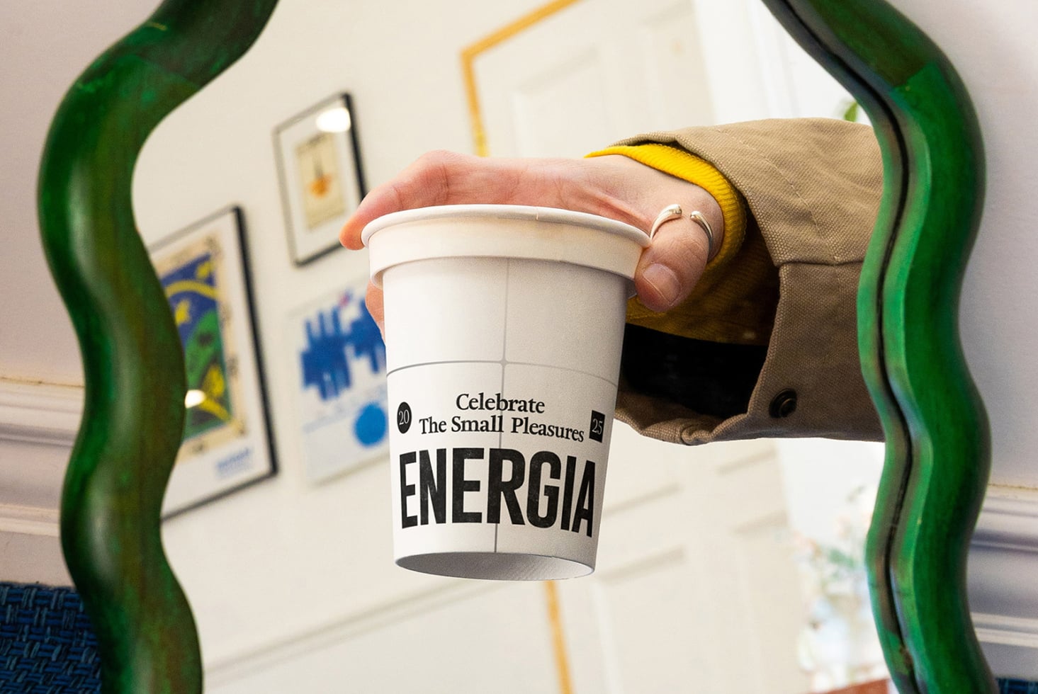White cup held between hands against green mirror frame in casual home setting