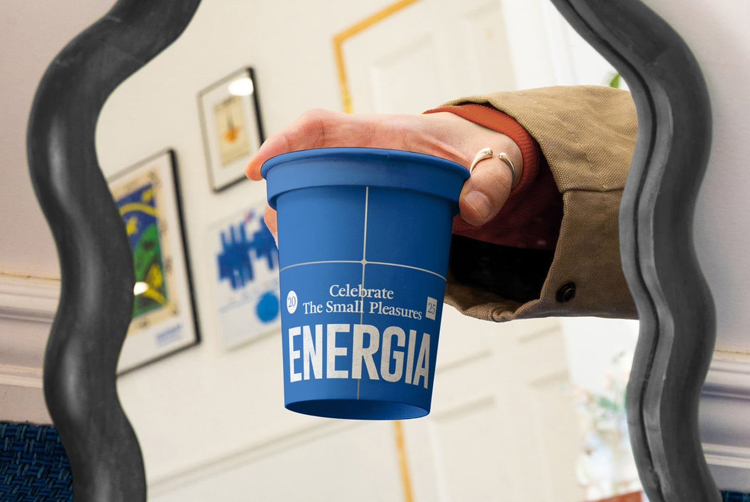 Hand holding blue Energia cup with straw framed by black chair arms in bright office