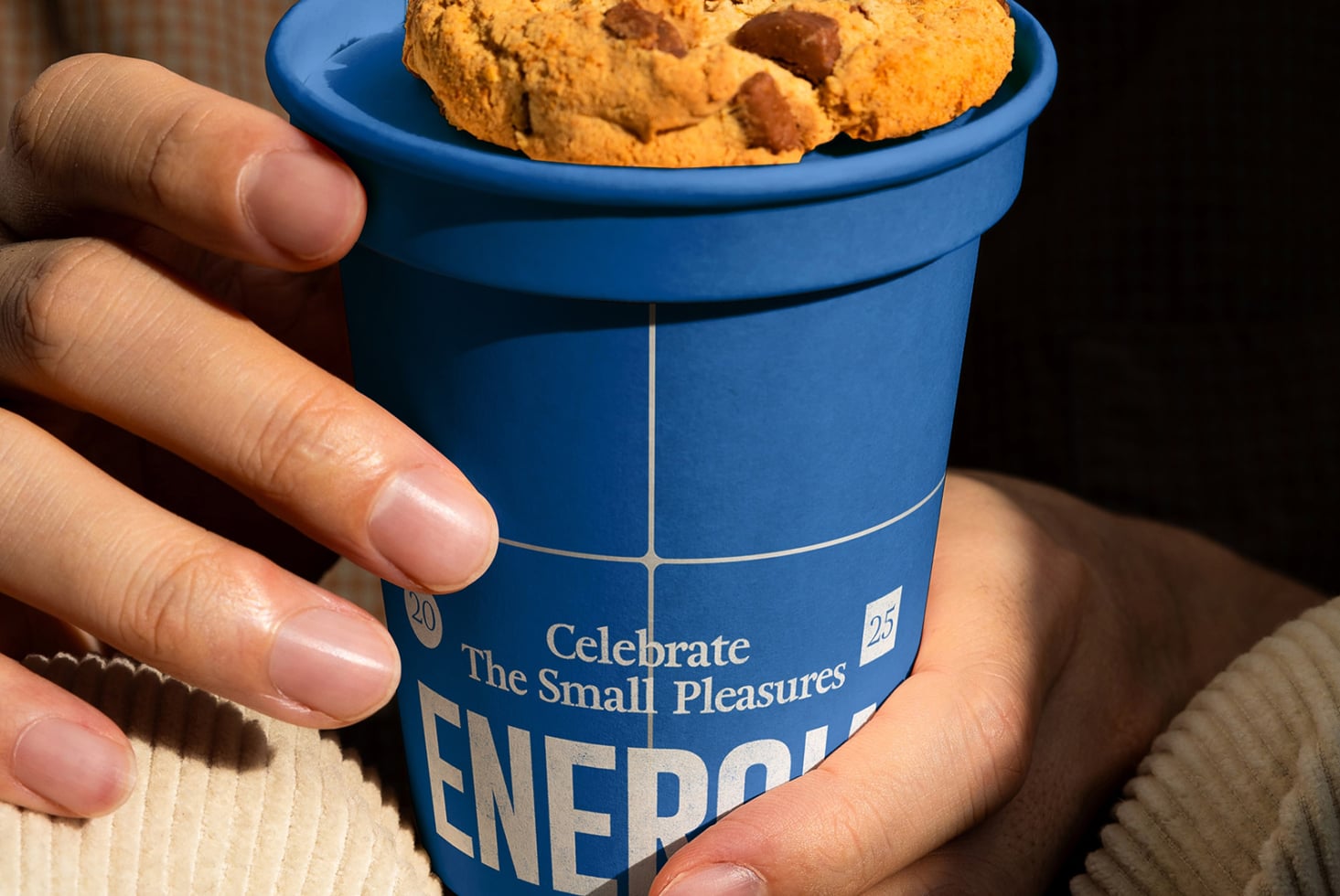Hand holding blue paper cup with cookies on top, Energia label visible on side