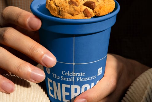 Hand holding blue paper cup with cookies on top, Energia label visible on side