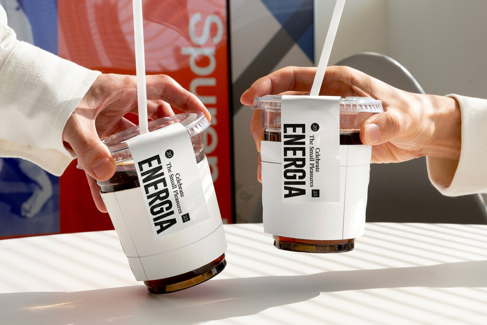Two clear cups with white ENERGIA labels, white straws, colorful branded boxes blurred behind