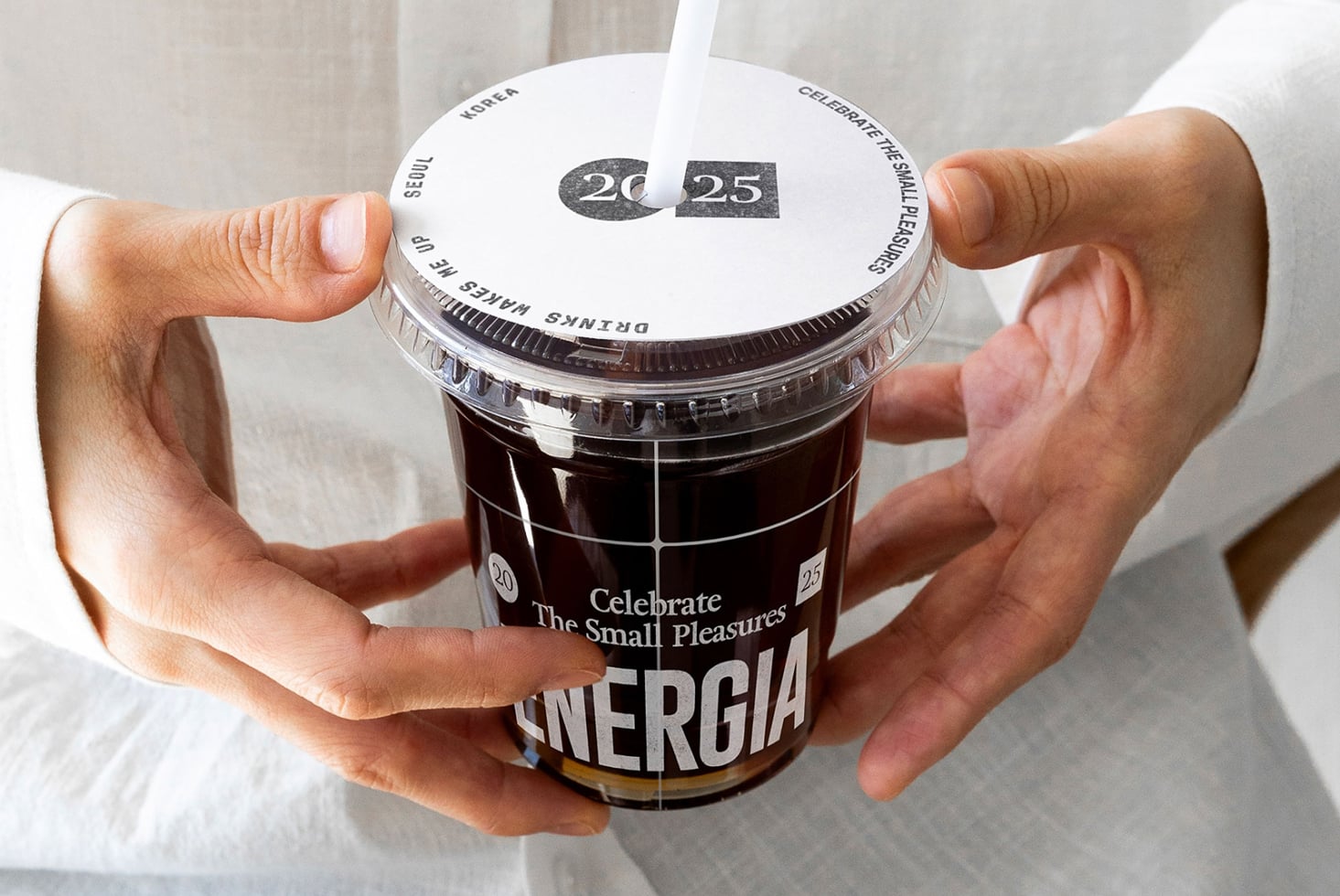 Hands holding beverage cup with white lid, date badge 20-25 visible