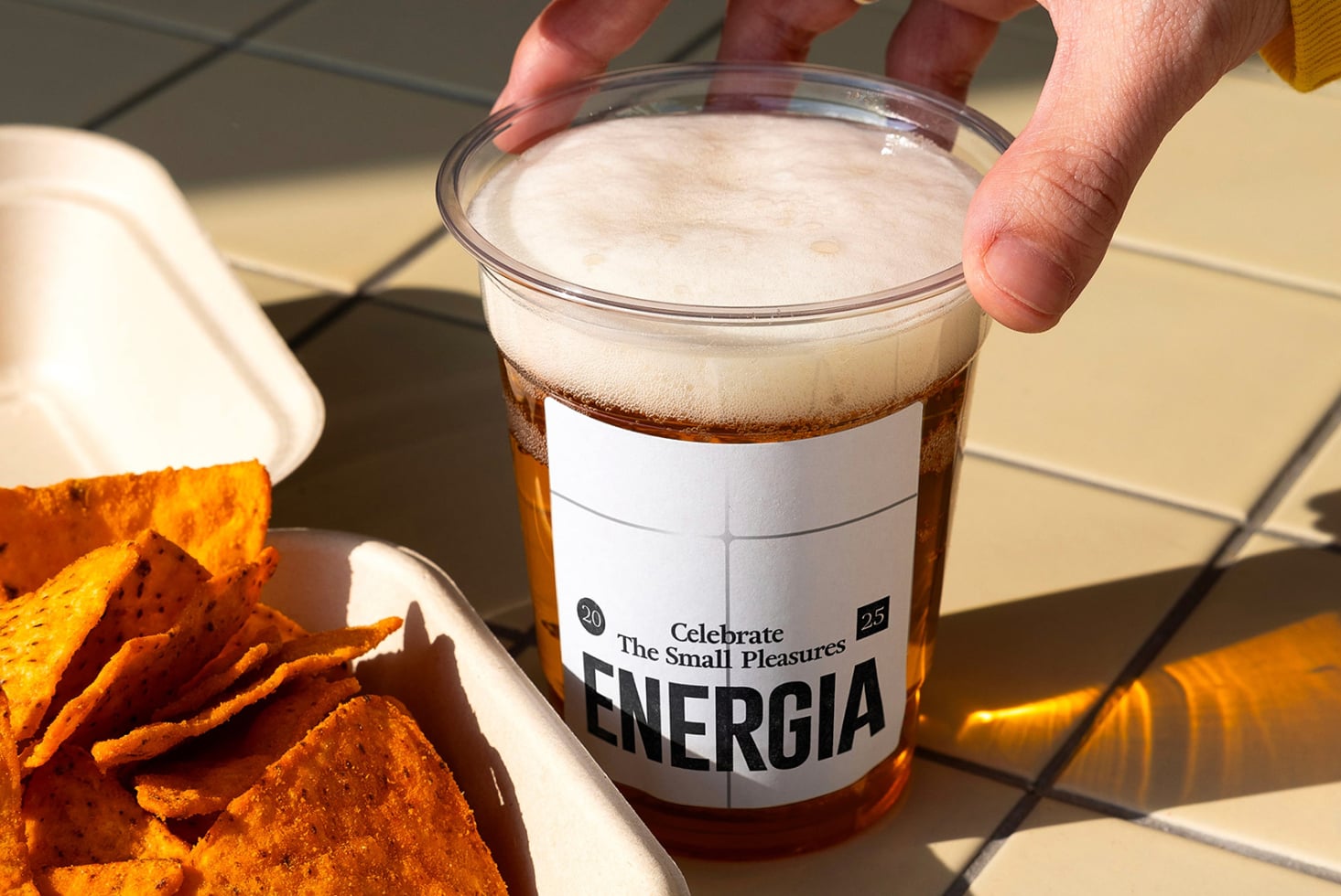 Close up of clear cup with white label held near orange snack chips in bowl