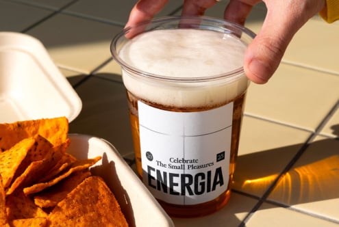 Close up of clear cup with white label held near orange snack chips in bowl