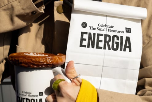 White paper bag mockup with Energia branding next to white mug with pastry